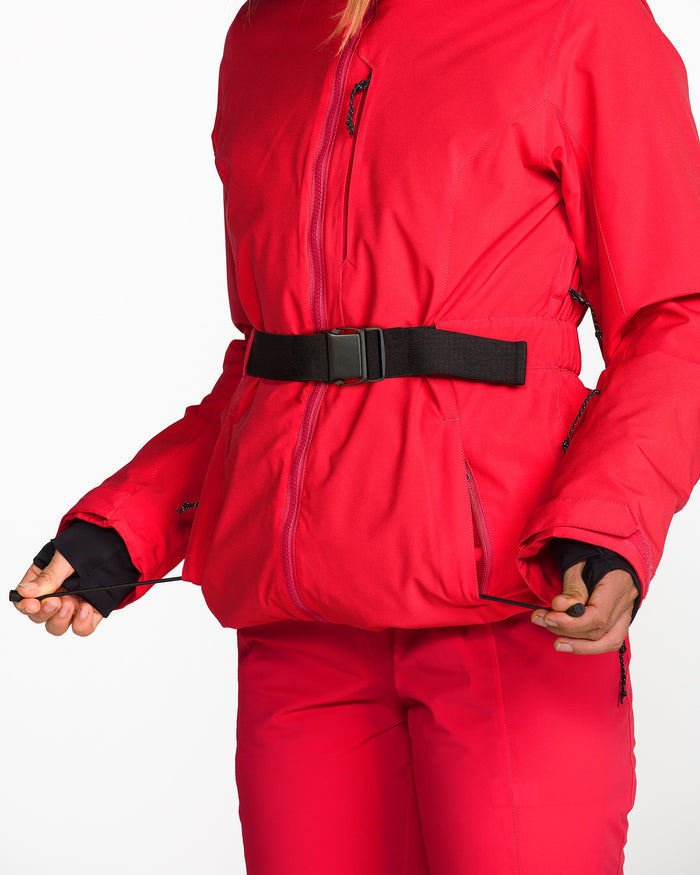 A person wears a vibrant red Volcom Women’s Alpine All Day Insulated Jacket with matching pants, adjusting the jacket’s hem drawstring. This 10K/10K V-Science jacket features a black belt, zippered pockets, and offers impressive 4-way stretch for all-day comfort. The background is plain white.