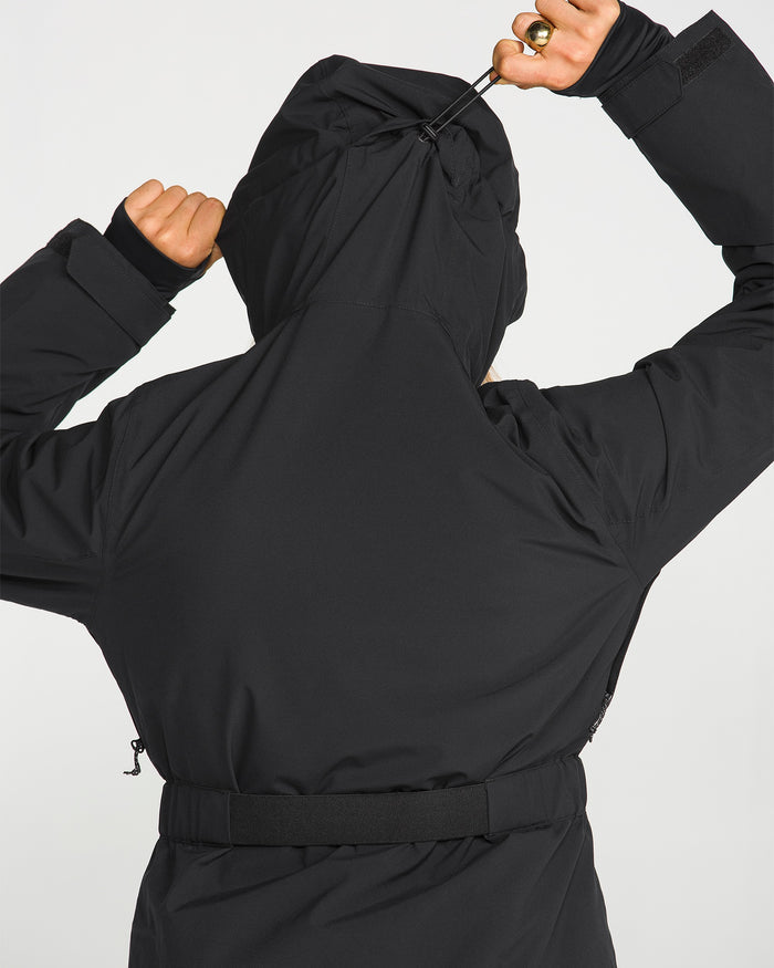 A person is seen from behind wearing the Volcom Women’s Alpine All Day Insulated Jacket in black, adjusting the fit by pulling on the drawstring at the back of the hood.