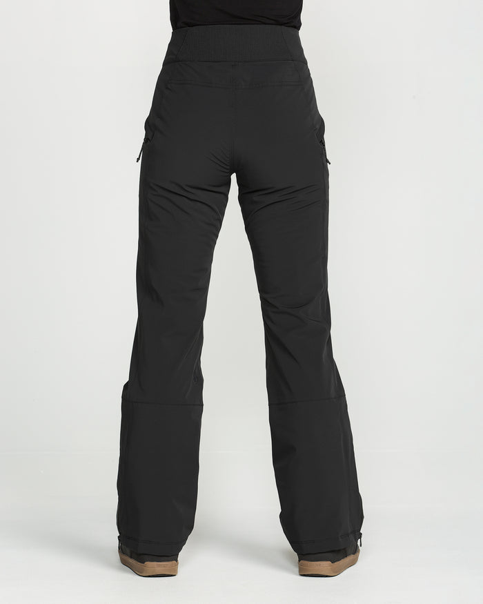 A person wearing the Volcom Women’s Alpine All Day Insulated Pants—high-waisted, black, wide-leg pants with a high-rise fit—and brown shoes is standing against a plain white background, facing away from the camera.