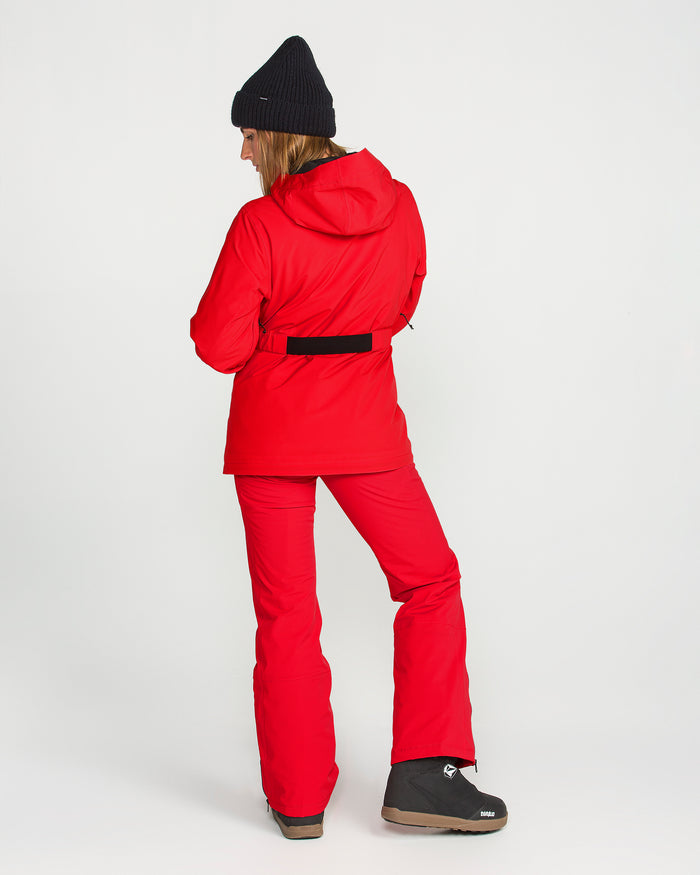 A person wearing a red winter jacket, Volcom Women’s Alpine All Day Insulated Pants with a high-rise fit, black beanie, and black boots stands facing away and looking over their left shoulder against a plain white background. The pants offer 4-way ultra stretch for comfort and freedom of movement.