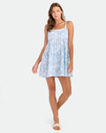 A woman in the Volcom Women's Beachmoonstone dress and beige sandals stands against a white background, smiling gently with one hand by her side and the other slightly raised.
