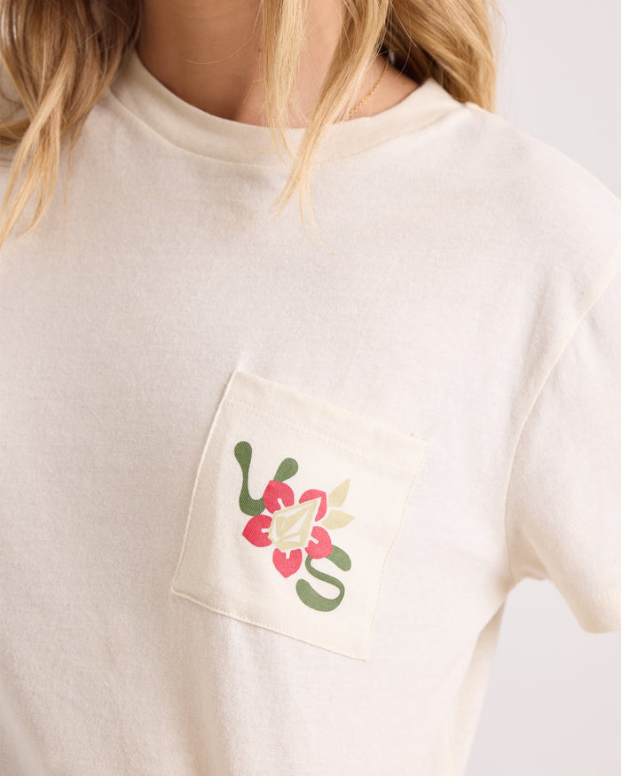 A woman is shown wearing the Volcom Women's Bite Club Pocket Dial Tee—an off-white 100% cotton short-sleeve knit top featuring a vibrant floral and leaf design in red, green, and beige on the pocket. Only her upper torso and part of her face and hair are visible, emphasizing this stylish tee.
