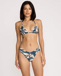 A woman with medium-length dark hair models the Volcom Women's Bloom Halter Triangle Bikini Top, featuring a light floral pattern, against a plain light background while looking at the camera with a neutral expression.