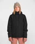 A person wearing the Volcom Women’s Bolt Insulated Jacket in black—ideal for staying warm in cold weather—along with a tan knit beanie and light brown gloves stands facing forward against a plain white background, looking slightly upward and to the side.