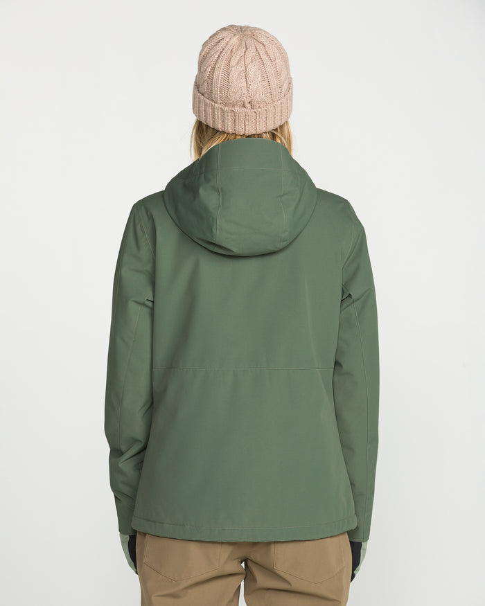 A person wearing a green Volcom Women’s Bolt Insulated Jacket with a hood, tan pants, and a light pink knit beanie stands facing away against a plain white background, showcasing both style and recycled warmth.