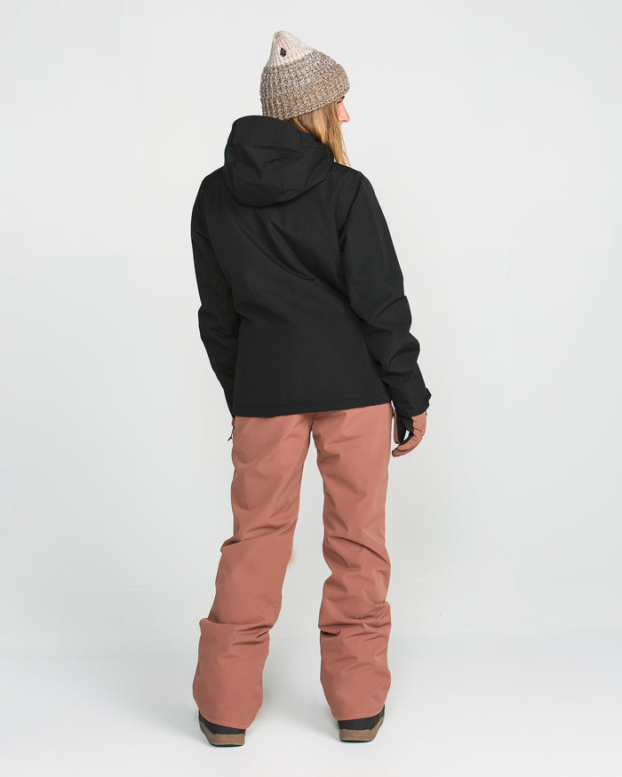A person stands facing away against a plain white background, wearing a gray knit beanie, loose pinkish-brown snow pants with black shoes, and the Volcom Women’s Bolt Insulated Jacket in black featuring Zip Tech.