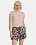 A woman with short blonde hair models Volcom's Women's Boss Beach Shorts, featuring a colorful pink and green tropical floral pattern, paired with a light pink short-sleeve top, against a plain white background.