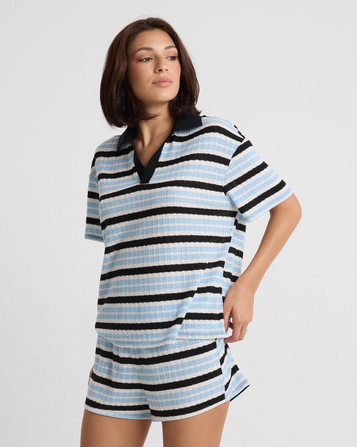 A woman wears Volcom Women's Coco Ho Crochet Shorts and a relaxed fit, short-sleeve, collared shirt in Blue Wave stripes. She stands against a white background with one hand on her hip and a relaxed expression.