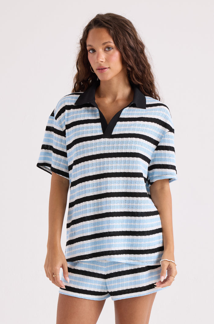 A woman with long brown hair models Volcom's Women's Coco Ho Crochet Shorts, showcasing a relaxed fit and horizontal blue, black, and white stripes against a plain light background.