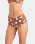 A model wears Volcom Women's Coco Retro Bloom Surf Shorts featuring a brown and white floral pattern for cheeky coverage, matching the bra, shown from chest to upper thighs against a plain light background.