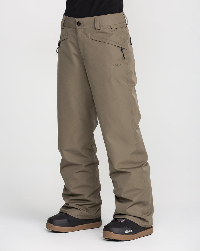 A person wearing Volcom Women’s Coldfront Insulated Baggy Pants in olive green, featuring zippered pockets, paired with black winter boots and standing against a plain white background. The baggy style of the pants offers added comfort and warmth, with only the lower half of the body shown.
