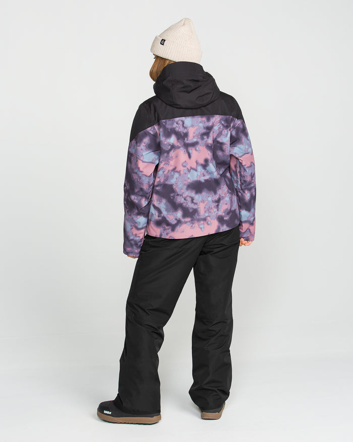 A person is seen from behind against a plain white background, wearing a beige beanie, a black and purple tie-dye jacket featuring V-Science 2-Layer technology, and Volcom Women’s Coldfront Insulated Baggy Pants in black with recycled insulation.