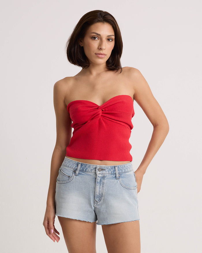 A woman with straight brown hair wears the Volcom Women's Cruz Control strapless red top and high-rise chambray denim shorts, standing against a plain white background and looking at the camera with a neutral expression.