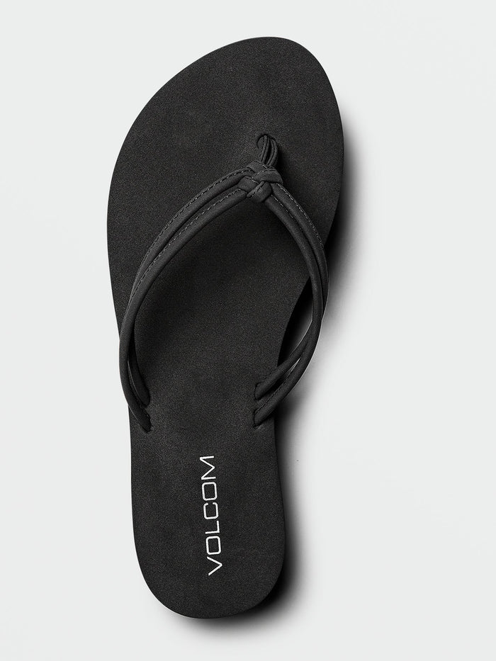 The Volcom Women's Forever And Ever II black flip-flop sandal features thin synthetic leather straps and "VOLCOM" printed in white on the footbed, along with molded arch support for extra comfort, displayed on a light background.
