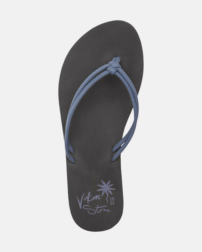 The Volcom Women's Forever And Ever II is a black flip-flop sandal with blue straps, featuring a palm tree graphic and "Volcom Stone 1991" printed in light purple near the heel.