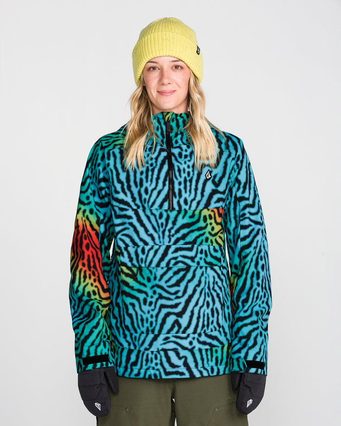 A person wearing a yellow beanie, black gloves, and the Volcom Women’s Harlan Pullover—a blue, green, and red zebra-striped jacket featuring V-Science 2-Layer construction and PFAS-free DWR—stands facing forward against a plain white background.