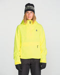 Wearing the Volcom Women’s Harlan Pullover in yellow, paired with black pants, gloves, and a black beanie, a person stands facing forward against a plain light background.