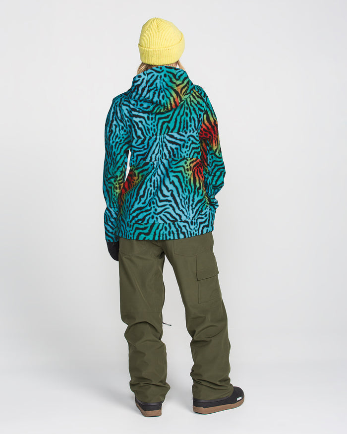 A person facing away, wearing a yellow beanie, green cargo pants, black boots, and the Volcom Women’s Harlan Pullover—a blue and red patterned jacket featuring V-Science 2-Layer technology—stands against a plain white background.