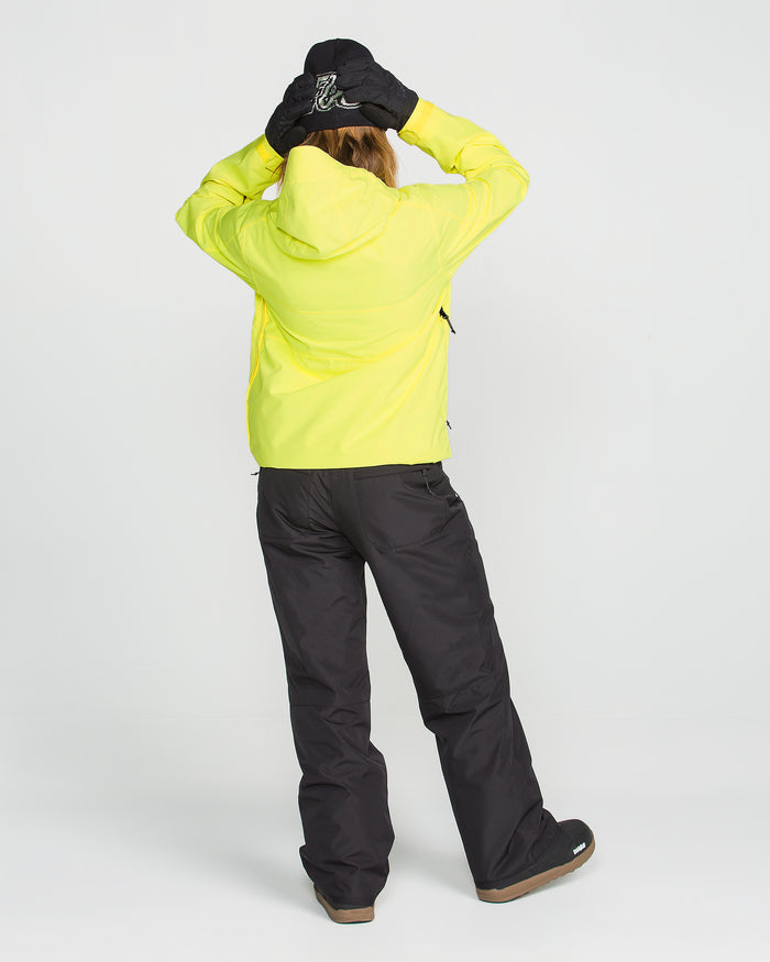 A person is seen from behind, standing against a plain white background with their hands on their head, wearing the Volcom Women’s Harlan Pullover in yellow—a waterproof jacket featuring a recycled shell—paired with black pants and black gloves.