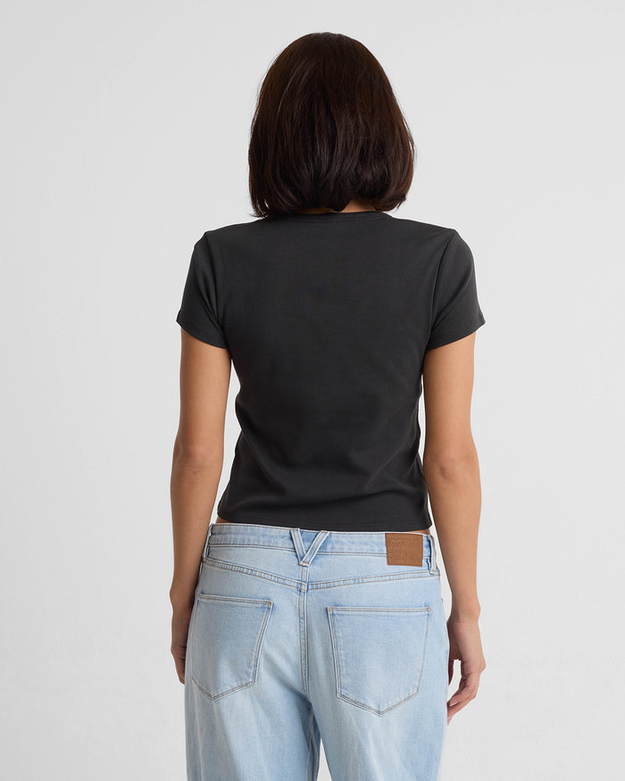 A woman with shoulder-length dark hair, seen from behind, wears the Volcom Women's Have A Clue Tee in black and light blue jeans against a plain white background.