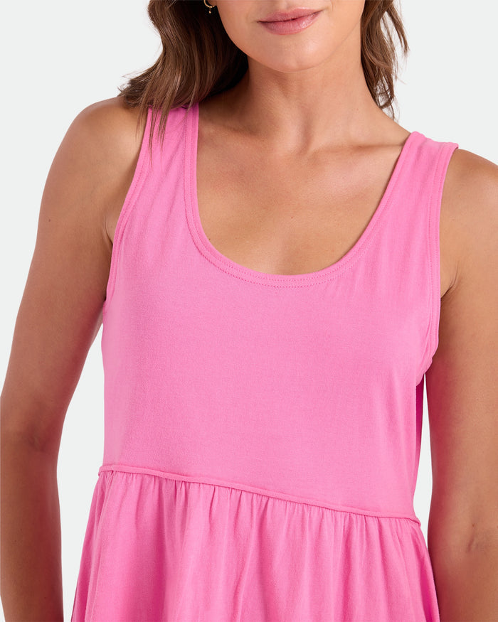 A woman models the Volcom Women's Hi Lo Tide Dress, a sleeveless, loose-fit pink mini dress. She smiles softly, her brown hair on her shoulder. The image is cropped from shoulders to mid-torso against a plain light background.