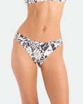A person models the Volcom Women's Hibiscus Diamond Midrise Skimpy Reversible Bikini Bottom, featuring a black and white floral pattern, shown from mid-torso to upper thighs against a plain background.