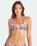 A woman with long brown hair models the Volcom Women's Hibiscus Diamond Reversible Triangle Top with adjustable ties and matching bottoms in a black and white floral print, standing against a plain background and smiling at the camera.