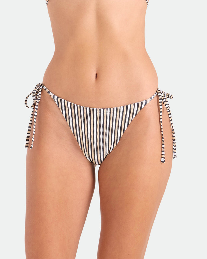 A person models the Volcom Women's Hibiscus Diamond Tie Side Full Reversible Bikini Bottom, made from recycled nylon, in black and white against a plain light background. The image is cropped to show the torso and upper thighs.