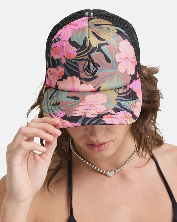 A person wearing the Volcom Women's Into Paradise Hat, featuring a black floral design with pink flowers, pulls the brim over their eyes. They pair it with a heart-shaped necklace and a black top.