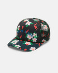 The Volcom Women's Into Paradise Trucker is a black mesh hat with a floral and strawberry pattern, featuring white flowers, red strawberries, and blue "BLOOM STORM" text on the foam front.
