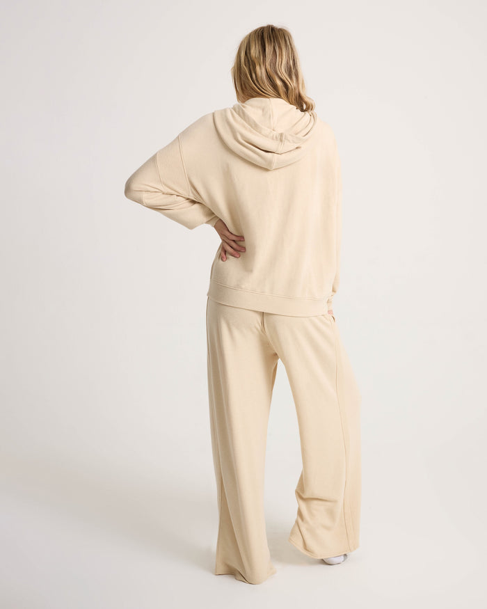 A person with long blonde hair stands facing away, wearing the Volcom Women's Lil Frenchie Zip Hoodie against a plain light background.