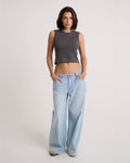A woman stands against a plain background, wearing the Volcom Women's Mary Mack Tank and light blue wide-leg jeans, with her hands in her pockets.