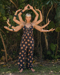 A woman stands barefoot outdoors in the Volcom Women's Midnite Ramble Dress. Behind her, people extend their arms so she appears to have many arms like a Hindu deity, with lush greenery all around.