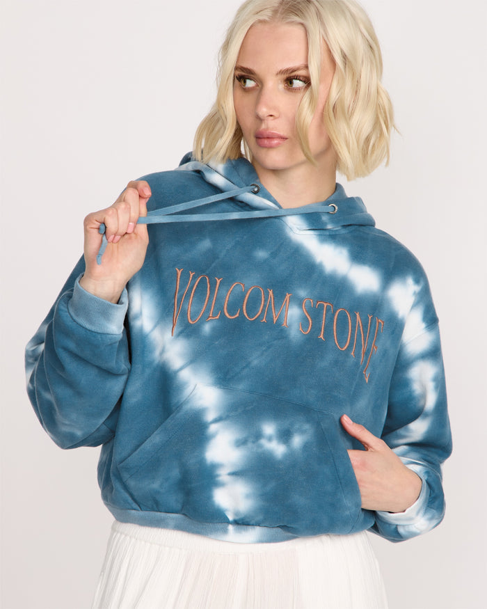 A woman with short blonde hair wears the Volcom Women's New Tie Dye Hoodie in blue and white, holding one drawstring and looking off to the side with a neutral expression.
