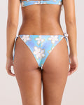 A woman is shown from the back wearing the Volcom Women's Ocean Haze Tie Cheekiini, a blue bikini with white floral patterns and side ties, against a plain background.