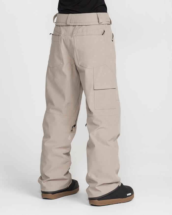 A person is shown from the back against a plain white background, wearing Volcom Women’s Pollock Baggy Pants in light beige—with multiple cargo pockets—and black shoes.