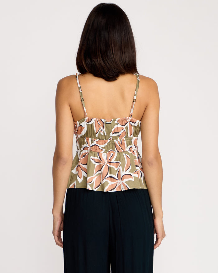 A woman with shoulder-length dark hair is seen from the back, wearing the Volcom Women's Psychonic Cami with a floral print and adjustable straps, paired with black pants against a plain white background.