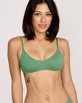 A woman with shoulder-length dark hair models the Volcom Women's Pucker Up Scoop Crop Bikini Top in green, made from recycled nylon with removable cups. Against a light background, she reveals a butterfly tattoo and smiles gently at the camera.