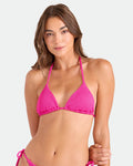 A woman with long brown hair wears the Volcom Women's Pucker Up Triangle Top in bright pink, made from recycled materials, posing against a plain light background and looking at the camera with a slight smile.