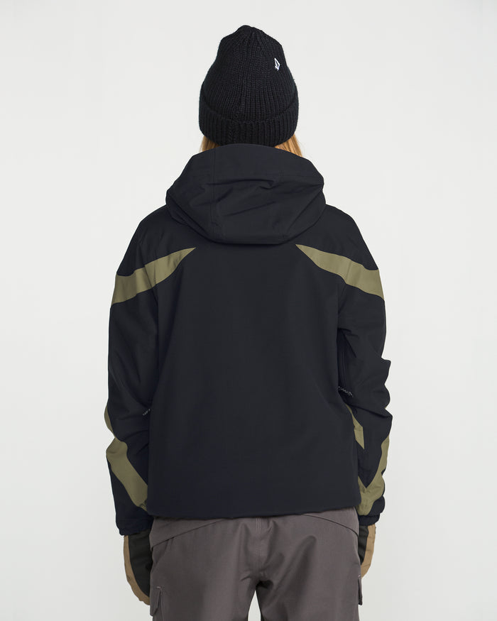 A person stands facing away against a plain white background, wearing the Volcom Women’s Shelter 3D Stretch Jacket in black with olive green accents and low-loft insulation, paired with a black beanie and gray pants.