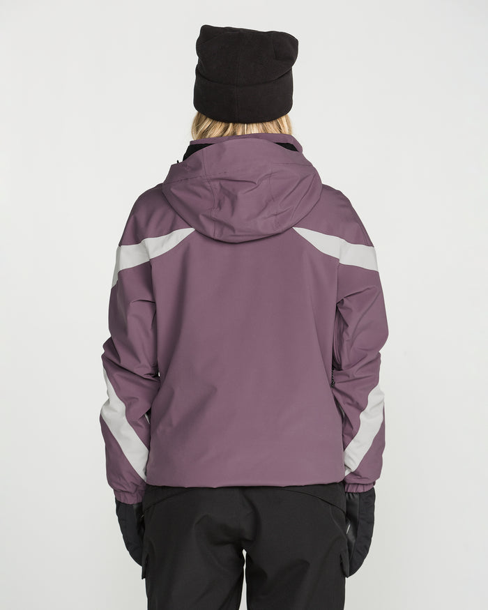A person is seen from behind against a plain white background, wearing the Volcom Women’s Shelter 3D Stretch Jacket in purple, along with a black beanie, black gloves, and black pants.