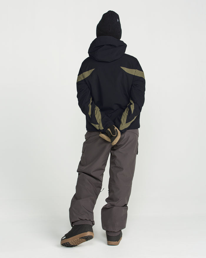 A person in winter clothing stands with their back to the camera, hands clasped behind. Ready for chilly weather, they wear a black beanie and the Volcom Women’s Shelter 3D Stretch Jacket—black with green accents and featuring low-loft insulation for warmth without bulk. Brown pants and brown shoes complete the look, all set against a plain white background.