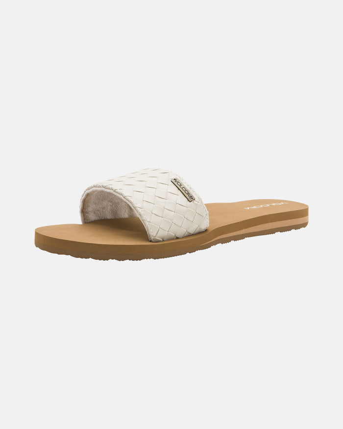 The Volcom Women's Simple Slides Braid Sandals feature a tan sole and a wide, woven white strap with a small metallic brand tag, shown against a plain white background.