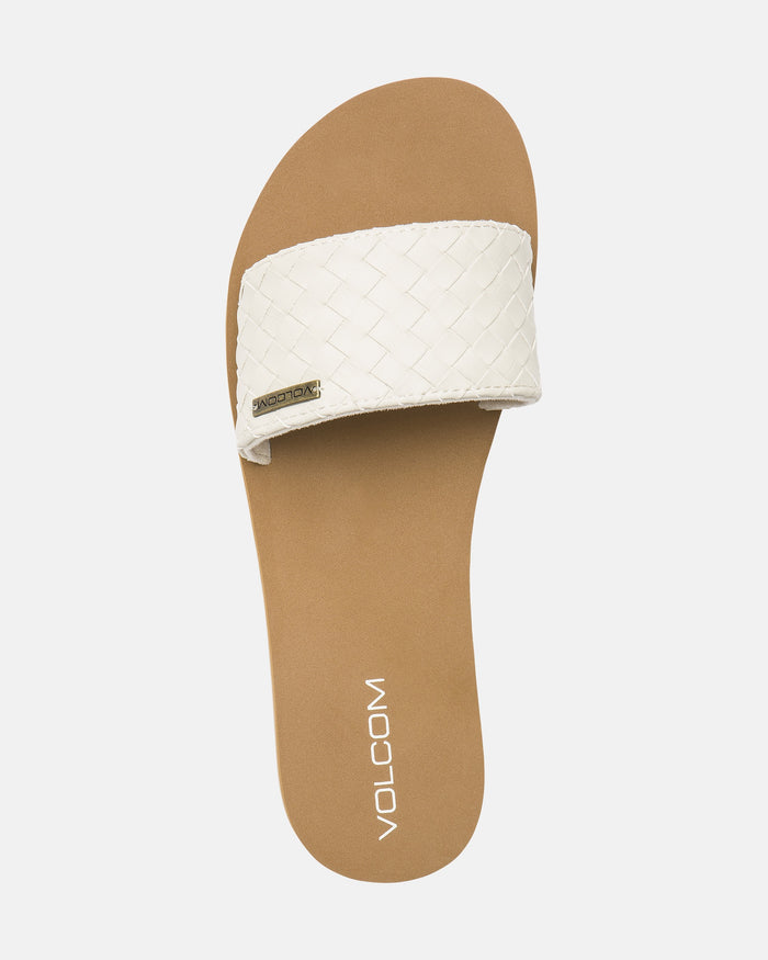 A single Women's Simple Slides Braid Sandal by Volcom, featuring a tan sole, woven white strap with small metallic Volcom logo tag, and "Volcom" printed in white on the brown footbed. Plain white background.