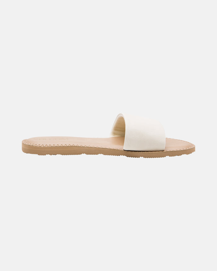 The Volcom Women's Simple Slide is a minimalist flat sandal with a light tan sole and a wide off-white strap, shown in side profile on a plain white background.