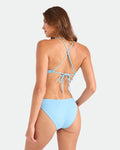 A woman wears the Volcom Women's Simply Seamless Hipster Full bikini in light blue, showcasing full coverage hipster bottoms and thin crisscross straps on top. Crafted from recycled nylon, she's seen from the back against a plain white background.