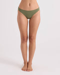 A woman stands barefoot against a plain background, wearing Volcom Women's Simply Seamless Hipster Full bikini bottoms in olive green. Her arms are out of frame, and her body is facing forward, showcasing the comfortable full coverage swimwear design.