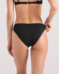A woman is seen from the back wearing the Volcom Women's Simply Seamless Midrise Skimpy bikini bottom and a matching black top made from recycled nylon, with a bracelet on one wrist against a plain light background.