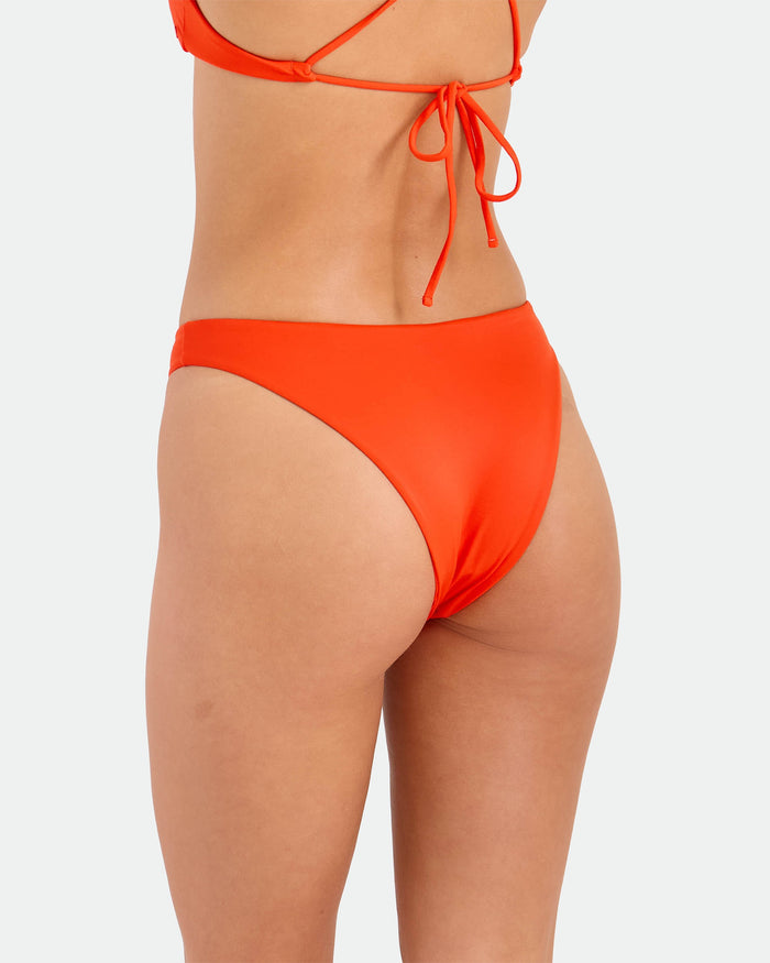 A woman is shown from the waist down, side and back, wearing the Volcom Women's Simply Seamless Midrise Skimpy bikini bottom with cheeky coverage and a matching top, set against a plain light background.