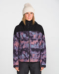A person wearing a cream knit beanie and the Volcom Women’s Steele Insulated Jacket—featuring a purple-and-black pattern with black shoulders—stands facing forward against a plain light background.